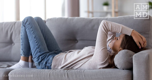 Woman laying on couch clutching head - Mercury Overload - Amy Myers MD®