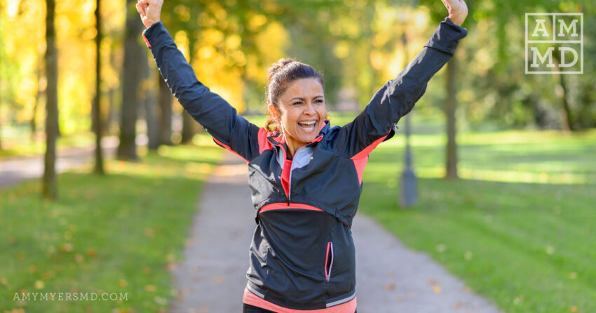 Smiling woman in windbreaker on trail with arms up - What are Endorphins & Why We Want Them - Amy Myers MD®