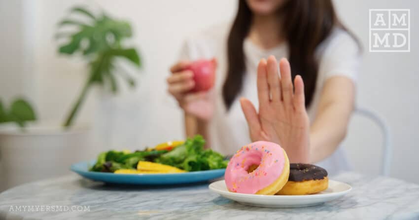 Woman pushing away donuts in favor of leafy greens - How to Stop Sugar Cravings - Amy Myers MD®