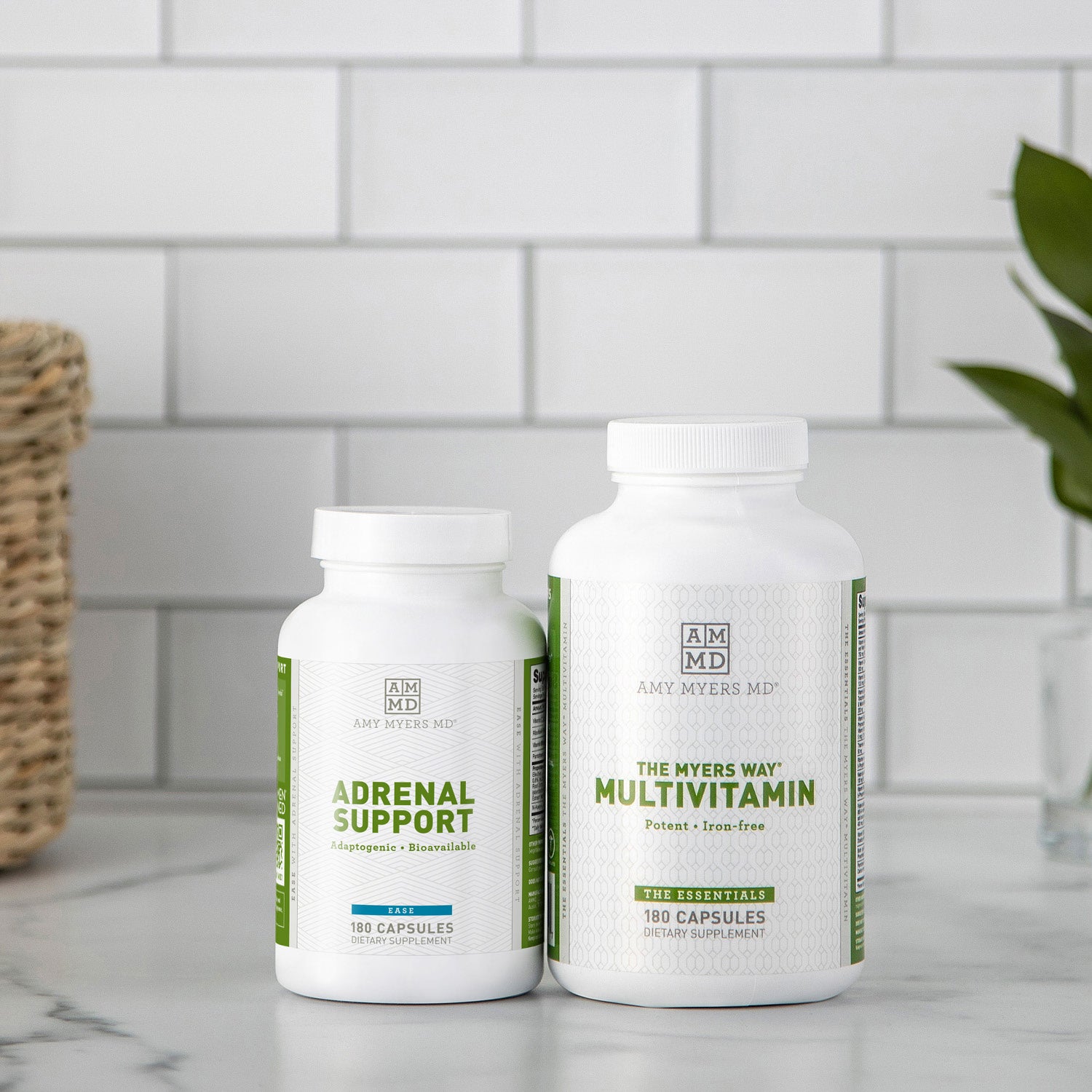 Adrenal Support capsule bottle next to a Multivitamin capsule bottle sitting on a white granite countertop with white tile background. 